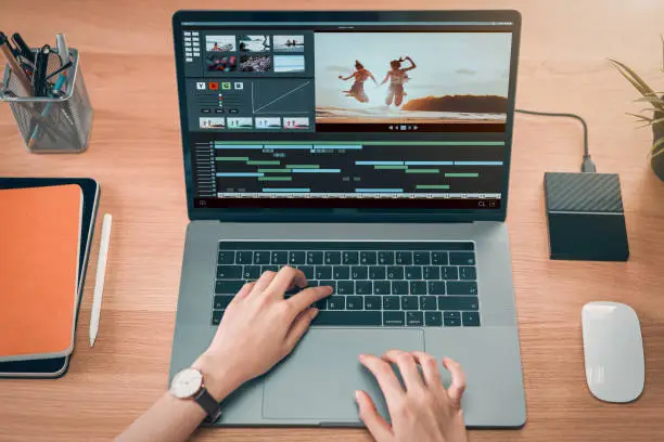Concept of simple operation of blogger and vlogger, hand using laptop on video editor works with footage on wooden table, camera and accessories on table.