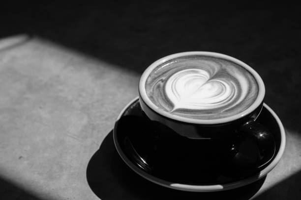 istock Black and white of coffee latte art with heart shape pattern on top on rustic table bar in morning light with copy space 1180898756