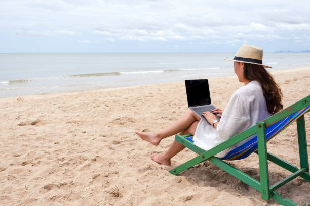 istock A woman using and typing on laptop computer on a beach chair 1180899782