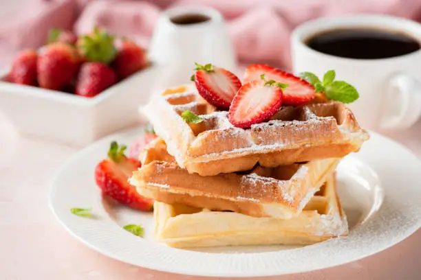 Belgian waffles with strawberry and powdered sugar on white plate, pink background