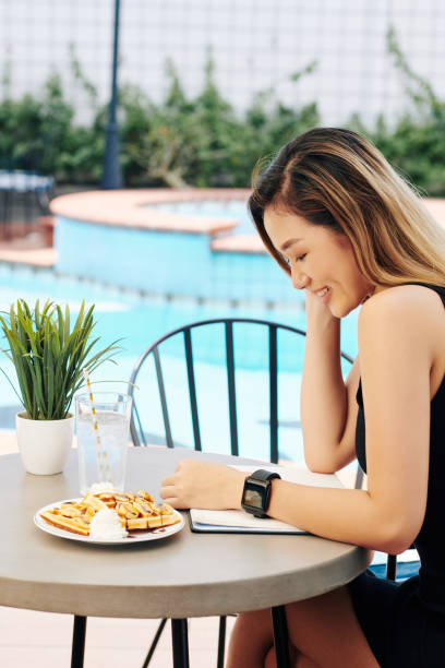 uśmiechnięta kobieta jedząca gofry i czytając książkę - waffle eating meal food and drink zdjęcia i obrazy z banku zdjęć