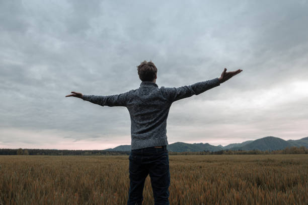 istock Young man standing in meadow with his arms open 1180915437