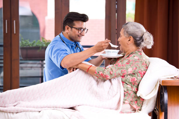 male nurse feeding food to senior patient on bed - senior adult nursing home eating home interior imagens e fotografias de stock