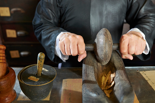 Hands of Asian traditional medicine practitioner grinding up dry herbs and roots in special boat tool