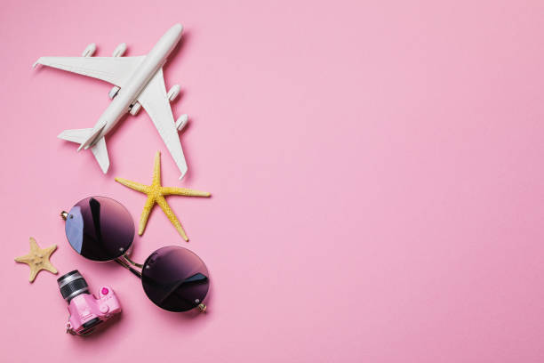 istock Beach accessories on a pink background with copy space. Vacation theme template. Airplane, glasses and a camera, top view 1180921888