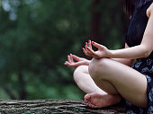 若い女性は、木材で瞑想、黒いドレスで脚、手と体の一部をクローズアップし、手に選択的な焦点、側面図。