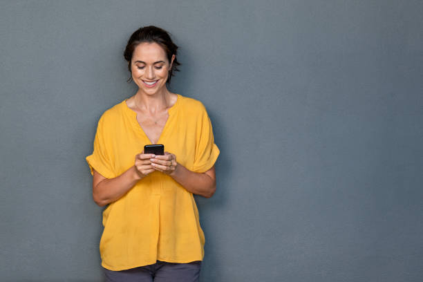 зр�елая латинская женщина с помощью смартфона на серой стене - mobile phone text telephone message стоковые фото и изображения