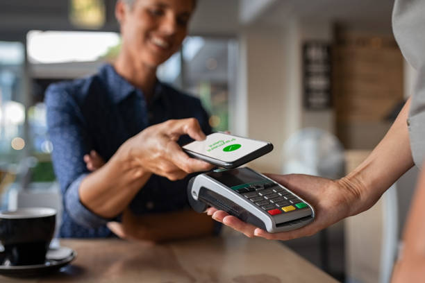 Woman paying using NFC technology Mature woman paying bill through smartphone using NFC technology in a restaurant. Satisfied customer paying through mobile phone using contactless technology. Close up hands of mobile payment at a coffee shop. mobile payment stock pictures, royalty-free photos & images