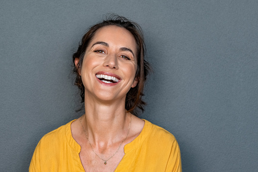Portrait of mature woman laughing against grey background. Successful middle aged woman in casual clothing with toothy smile looking at camera. Cheerful happy young beautiful latin lady smiling with copy space.