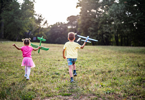 Cute little boy and girl playing with airplane toy on a field on sunset.