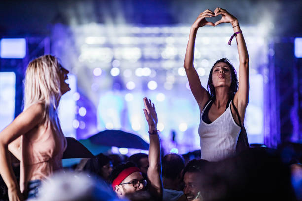femme espiègle affichant la forme de coeur sur le festival de musique la nuit. - music festival popular music concert music crowd photos et images de collection