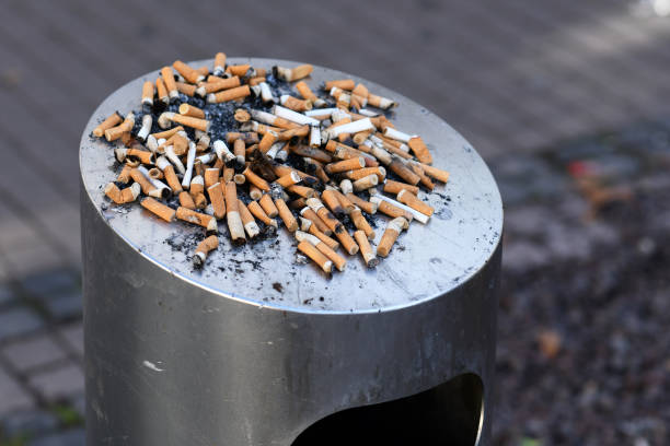 istock Many old cigarette stubs spilling over from ashtray of overflowing public trash bin 1180930136