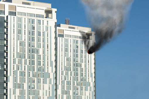 Skyscraper fire accident. Concept of firefighting problems at the height. Thick smoke billows from a window of apartment or office at high level