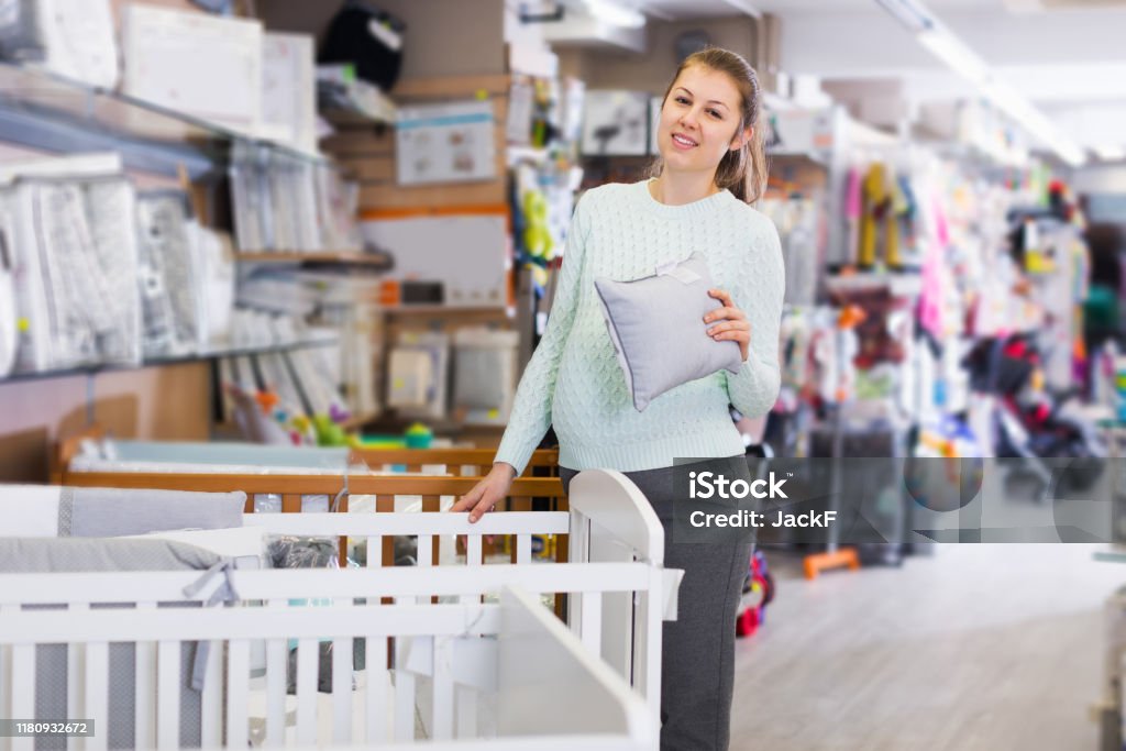 woman choosing pillow for crib happy woman is awating for baby and choosing pillow for crib in the shop. Store Stock Photo