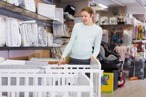 Pregnant woman is selecting baby crib in the shop.