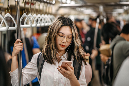 Young female student standing in subway train and text messaging on mobile phone