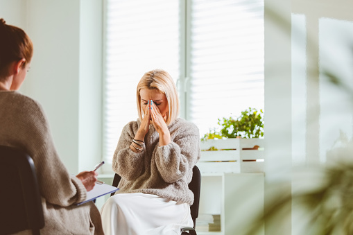 Sad mature female sharing problems with therapist. Mental health professional is with depressed mature woman. They are sitting at community center.