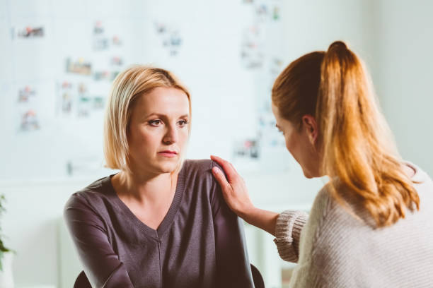 Female therapist consoling mid adult woman Psychotherapist consoling depressed mid adult woman. Sad female is looking at mental health professional during therapy session. They are sitting in community center. hand on shoulder photos stock pictures, royalty-free photos & images