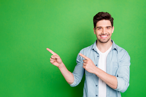 Foto de un hombre vendedor increíble en estado de ánimo excitado indicando dedo a espacio vacío aconsejando precios de compras frescos usar camisa de mezclilla casual de color verde aislado photo
