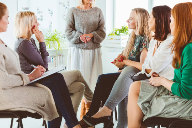 istock Female discussing with group in therapy session 1180947908