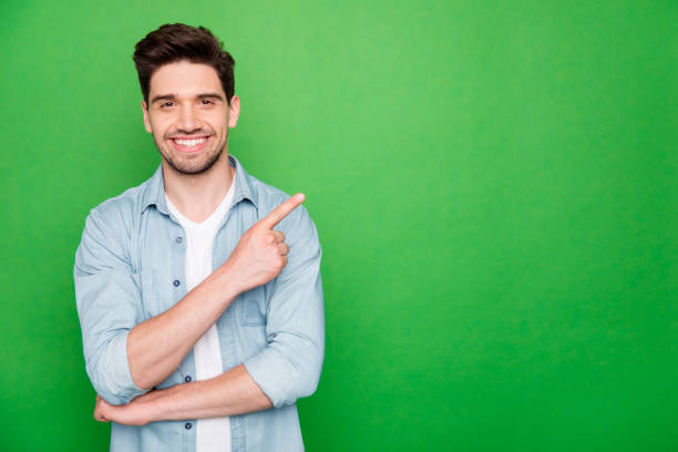 photo of positive cheerful attractive handsome man pointing at empty space with forefinger smiling toothily with bristle isolated over green color vivid background - people joy relaxation concentration imagens e fotografias de stock