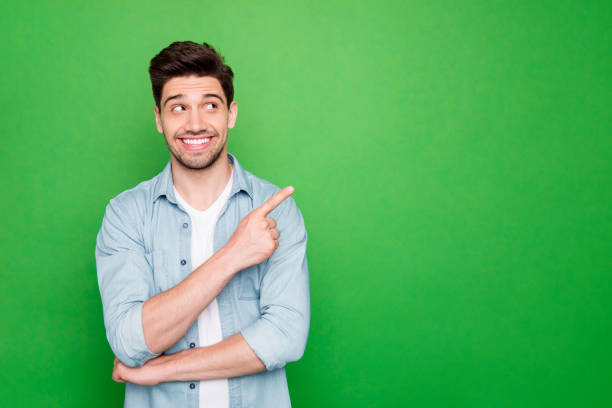 Photo of amazing salesman guy in excited mood indicating finger to empty space advising cool shopping prices wear casual denim shirt isolated green color background Photo of amazing salesman guy in excited mood indicating finger to empty, space advising cool shopping prices wear casual denim shirt isolated green color background directing photos stock pictures, royalty-free photos & images