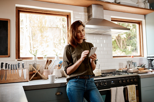 Cropped shot of an attractive young woman using a smartphone while standing in her kitchen at home