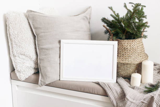 White blank wooden frame mockup with Christmas tree, candles, linen cushions and plaid on the white bench. Poster product design. Scandinavian home decor, nordic design. Winter festive concept. White blank wooden frame mockup with Christmas tree, candles, linen cushions and plaid on the white bench. Poster product design. Scandinavian home decor, nordic design, winter festive concept. pillow photos stock pictures, royalty-free photos & images