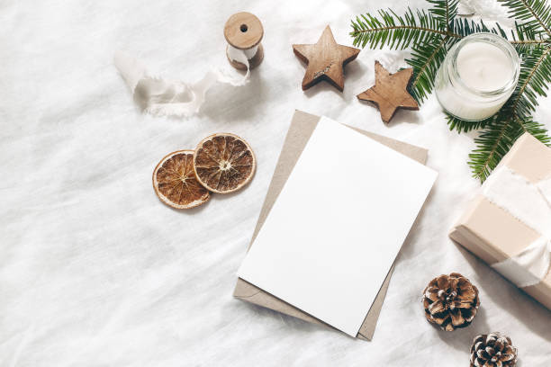 Christmas blank greeting card mock-up scene. Festive winter wedding composition. Craft envelope, pine cone, gift box, orange fruit slices and fir tree branch on white table, linen background. Flat lay. Christmas blank greeting card mock-up scene. Festive winter wedding composition. Craft envelope, pine cone, gift box, orange fruit slices and fir tree branch on white table, linen background, flat lay. winter still life stock pictures, royalty-free photos & images