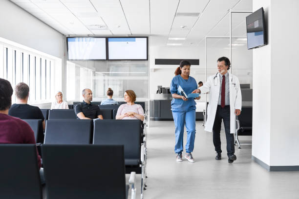 Doctor and nurse walking by patients in lobby Patients sitting in waiting room. Confident doctor and nurse are walking in corridor. They are in hospital. waiting room stock pictures, royalty-free photos & images