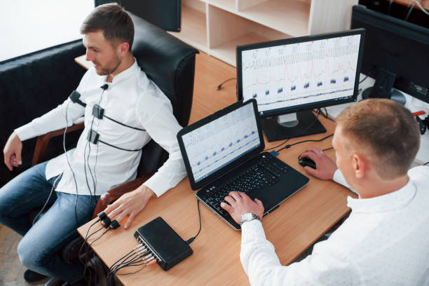 istock Are you ready. Suspicious man passes lie detector in the office. Asking questions. Polygraph test 1180957629