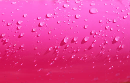 Bright pink inflatable paddling pool surface with water drops on it. Summer picture of swimming pool
