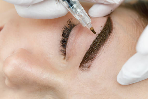 Permanent makeup, tattooing of eyebrows. Cosmetologist applying make up Permanent makeup, tattooing of eyebrows. Cosmetologist in white gloves applying make up with machine for woman in beauty salon durability stock pictures, royalty-free photos & images