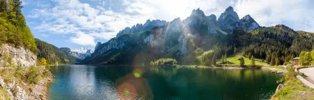 Photo of Famous Lake Gosau and Gosaukamm with Mount Dachstein. The sun is about to hide behind the high peaks while autumn is about to settle in with all the vibrant colors around the lake and hills.