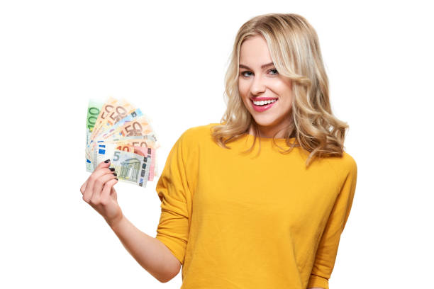 Young pretty woman in yellow sweater holding bunch of Euro banknotes, looking at camera and smiling, isolated on white background. stock photo