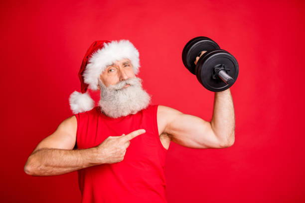 ritratto di sportivo fresco di babbo natale in cappellino con acconciatura bianca, tenendo manubri mostrano l'effetto fitness di routine indossando abbigliamento sportivo isolato su sfondo rosso - body building energy strength power foto e immagini stock