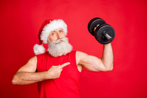 Portrait of cool santa claus sportsman in hat cap with white hairstyle, holding dumbbells show fitness effect routine wearing sportswear isolated over red background Portrait of cool santa claus sportsman in hat cap with white hairstyle, holding dumbbells show fitness effect routine wearing sportswear isolated over red background senior bodybuilders stock pictures, royalty-free photos & images