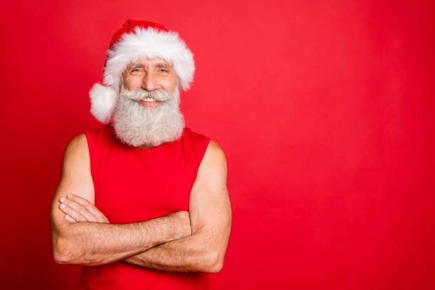 그의 손으로 매력적인 트렌디 한 산타 클로스 실제 코치의 초상화는 빨간 배경 위에 고립 된 니콜라스 모자 스포츠웨어를 입고 이빨이 많은 미소로 보고 교차했습니다. - men gray hair vitality healthy lifestyle 뉴스 사진 이미지