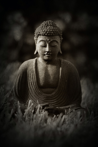 Statue of Buddha in meditation on black background. Mass-produced lava stone replica.