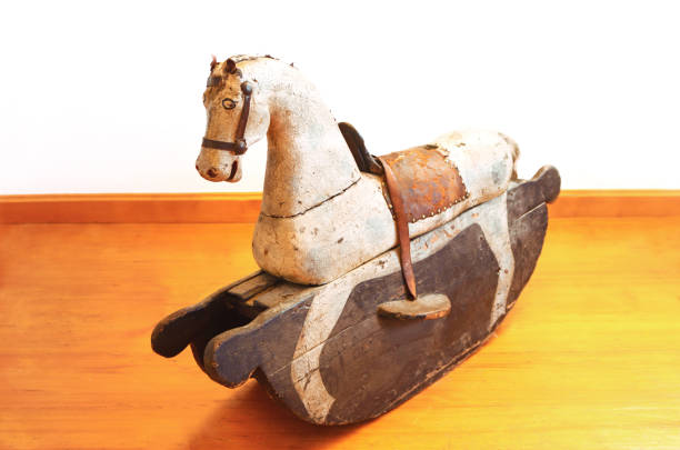 historic wooden rocking horse standing on an gold colored wooden floor in front of a white wall, retro background with copy space