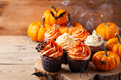 Halloween cupcakes and pumpkins on wooden background. Traditional sweets for holiday party.