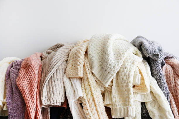 Bunch of sweaters of different material and knitting pattern in pile on gray sofa. stock photo