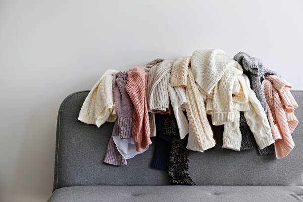 Bunch of sweaters of different material and knitting pattern in pile on gray sofa. Categorizing winter laundry concept. A messy pile of knitwear lying on grey textile sofa. Bunch of unfolded sweaters prepared for sorting. Close up copy space, background. unfolded stock pictures, royalty-free photos & images