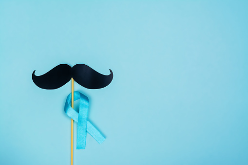 Movember background. Blue ribbon and black fake paper mustaches. Copy space