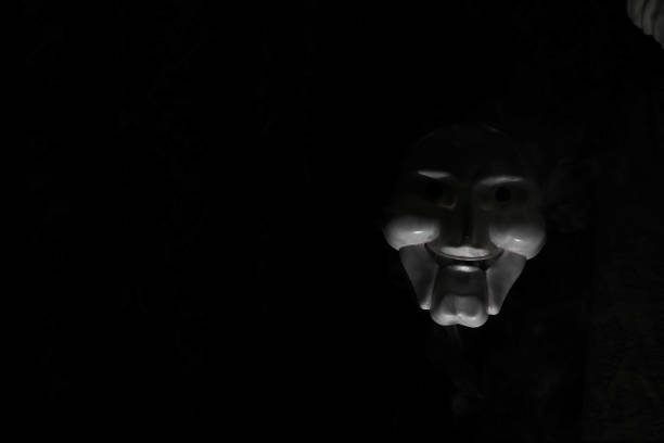 istock White scary mask on a black background with whites hand. 1180980857