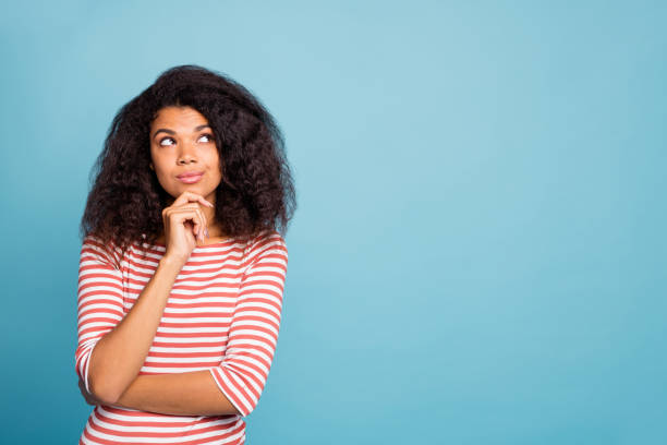 istock Photo of serious confident charming nice dark skinned youngster pondering over interesting plan touching her chin with hand looking at empty space isolated over blue vibrant color background 1180986197