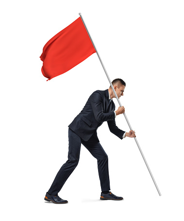 Side full length view of a young serious businessman planting a red flag on white background. Successful business. Top notch solutions. Getting work done.