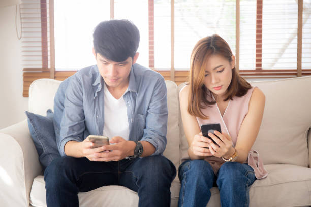 istock Young asian couple sitting on sofa with problem about relationship because addicts social network media together, asia family expression with looking phone with ignoring and indifferent. 1180989043