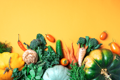 Autumn vegetables on trendy yellow background. Top view. Vegan and vegetarian diet, harvest concept. Ingredients for cooking - pumpkin, tomatoes, cucumber, pepper, kale, broccoli, celery.