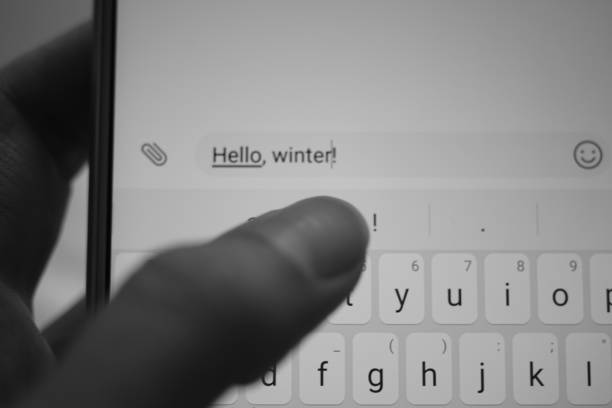 istock Female hand typing on a white smartphone a message Hello, winter. BW photo. 1180991416